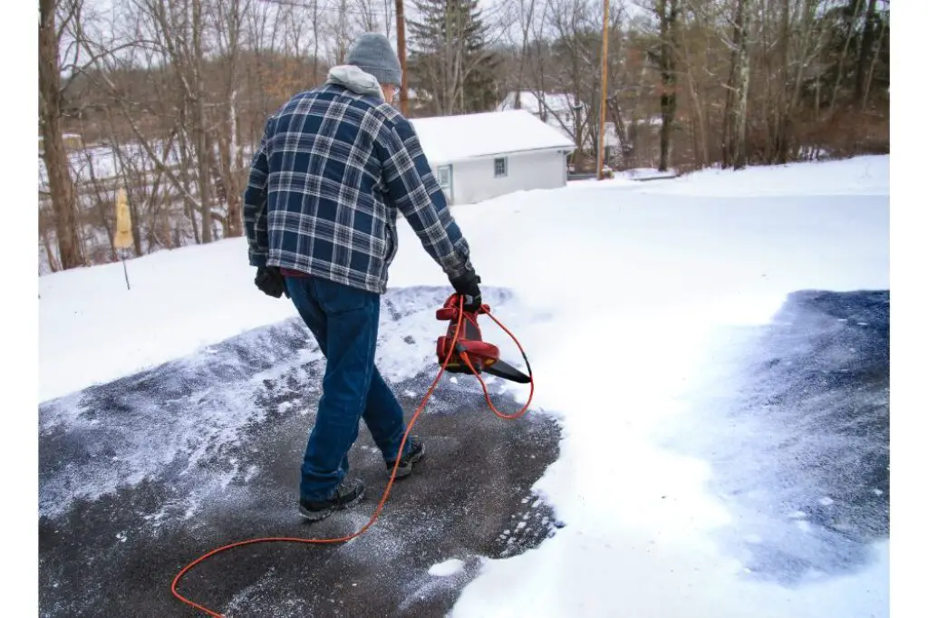 home owner uses a leaf blower to remove a light powdery snow 
